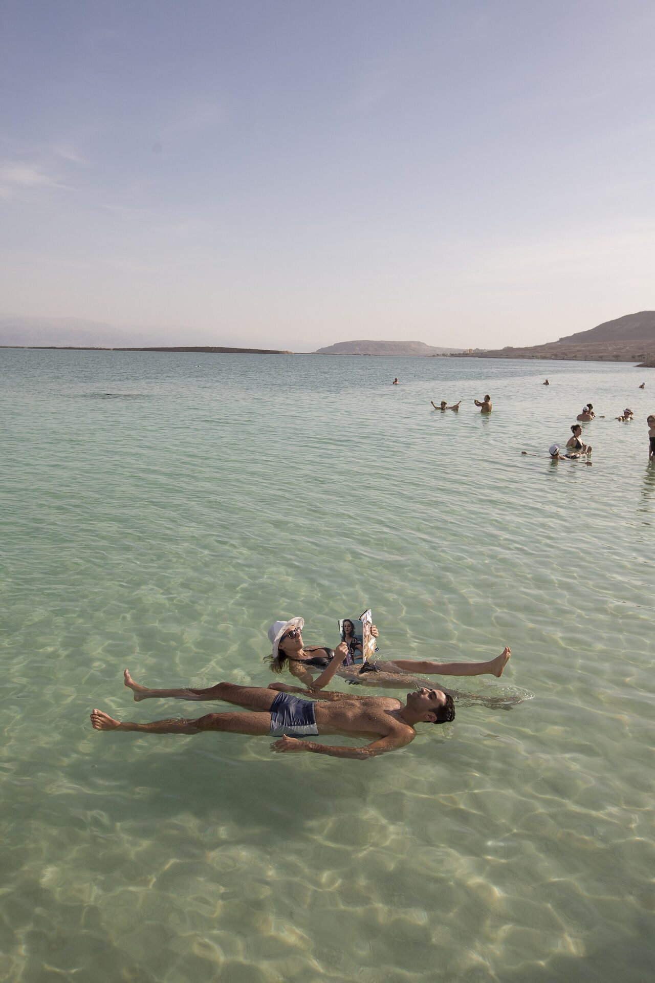 Bañistas flotando sin esfuerzo en las aguas azul turquesa del Mar Muerto con formaciones de sal en la orilla